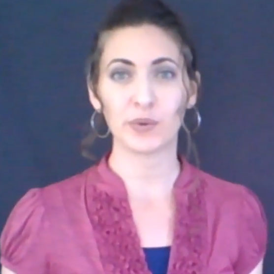 Woman with dark hair wearing hoop earrings and a magenta blouse, facing the camera against a dark background.