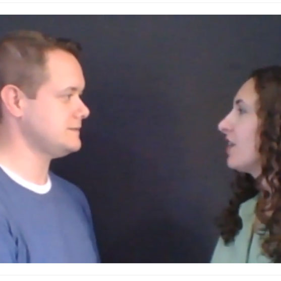 A man and a woman facing each other and talking against a dark background.